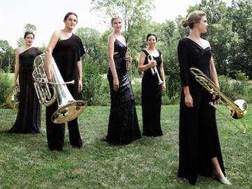five women in black dresses with brass instruments standing on lawn