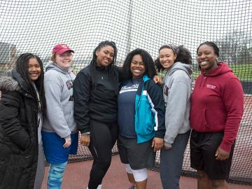 Six women posing by an athletics track