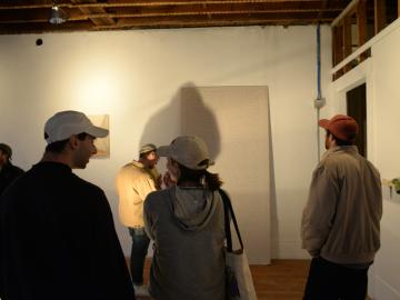 Gallery visitors look at art on the walls of a roughly finished room