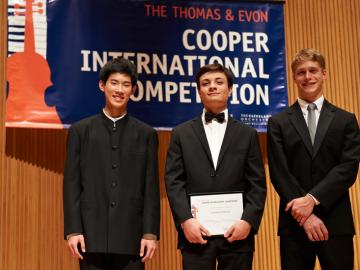 3 young men stand together on stage