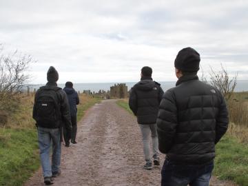 Four students in winter coats walk toward a castle.