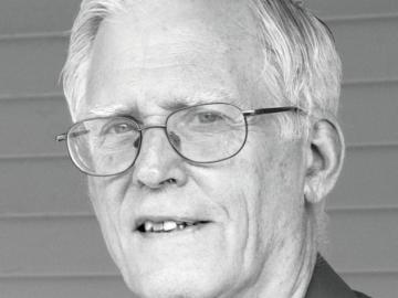 Alan Carroll poses in black and white photo wearing dark shirt.