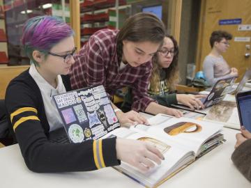 Two students look at  book with a picture of a large basket in it.