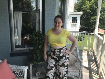 Ilana Ascher standing on porch wearing flowered pants and yellow shirt.