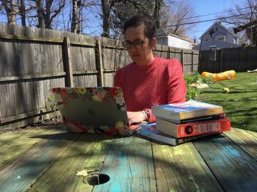 A woman types on a laptop in her backyard.