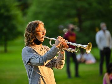 A student plays a trumpet in a park.
