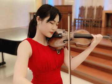 Asian girl in red dress plays a violin.