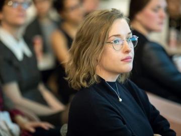 A girl wearing glasses sitting in an audience.