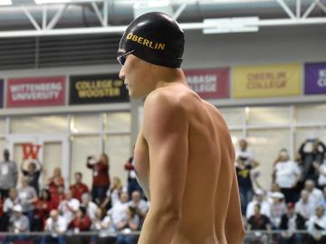 A male swimmer stands with a crowd behind him.