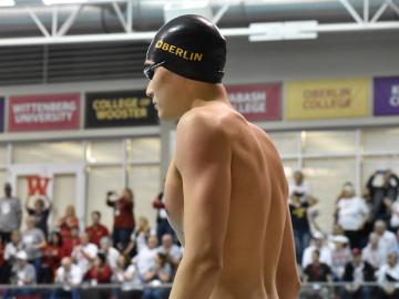A male swimmer stands with a crowd behind him.