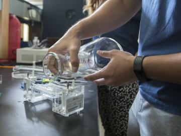 A science student pours liquid from a flask into an apparatus.