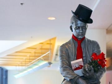 A statue of a man wearing a top hat and tie and carrying roses and a large diamond ring.