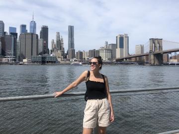 A woman stands next to a body of water across from downtown New York.