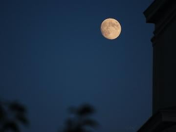 A full moon in a dark sky next to the silhouette of a building.