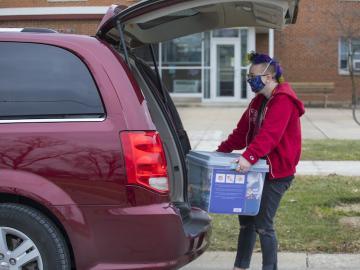 A student removes a large clear box from the trunk of a car.