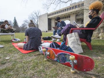Students sit ion the lawn and in chairs as they study outside,