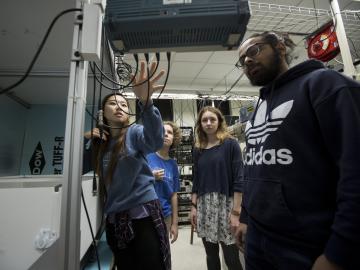 Four students stand in front of instruments in a physics lab.