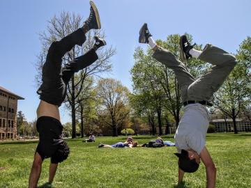 Two students do handstands on a lawn.