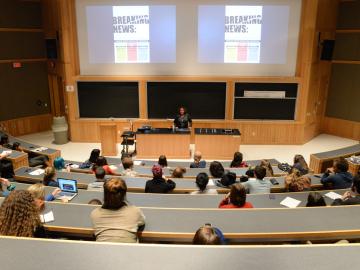 Lecture hall during a presentation. The words 'Breaking News' are visible on the screen behind the lecturer.