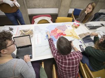 Students sit around a desk with computers and a large map.
