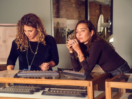 Two women working at a jewelry workbench, examining tools and materials together.