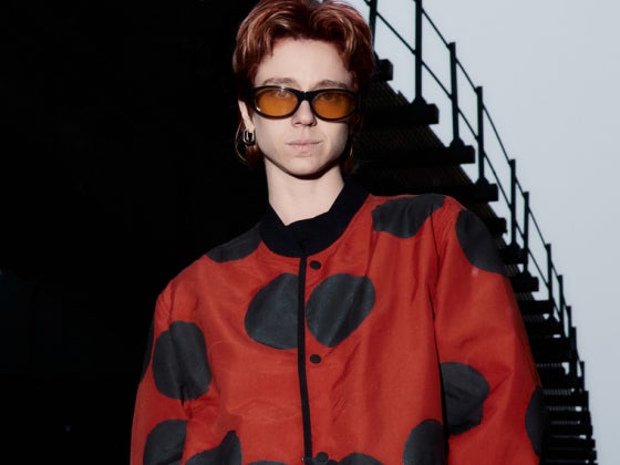 a person wearing a red jacket with black dots and orange-lens sunglasses
