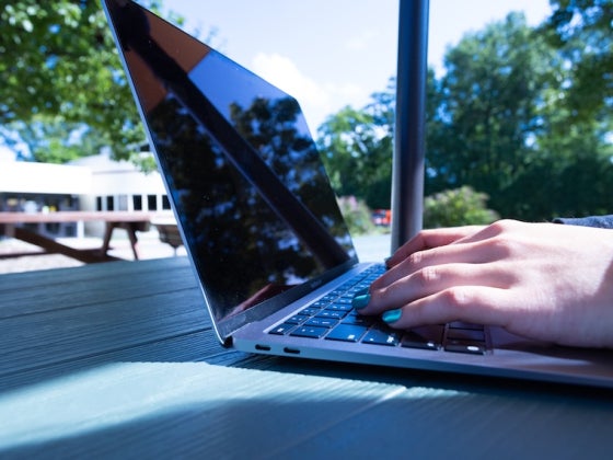 Hands typing on a laptop at an outdoor table.