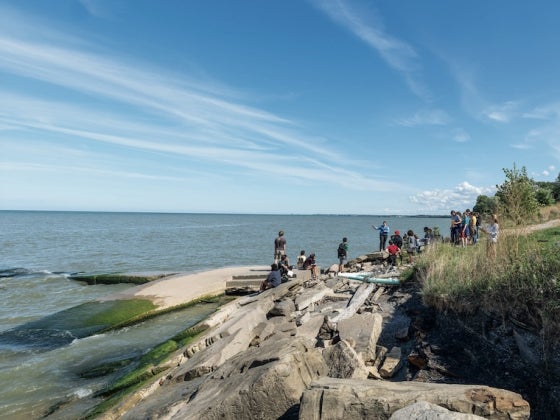 People standing on rocky shoreline beside a lake.