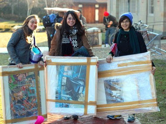 Students hold up framed art that is packed for transport.