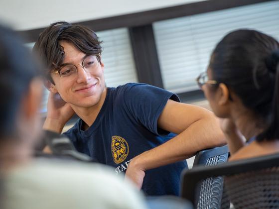 A student wearing glasses talking to another student in class.