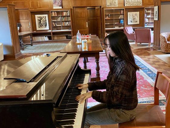 A student practices piano in a residential lounge.