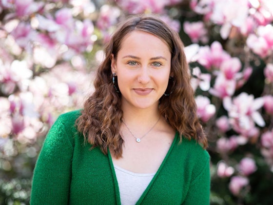 young woman in green sweater white blose standing in front of magnolia bush.