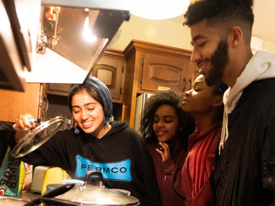 A small group of students peers into a pot on a stove.