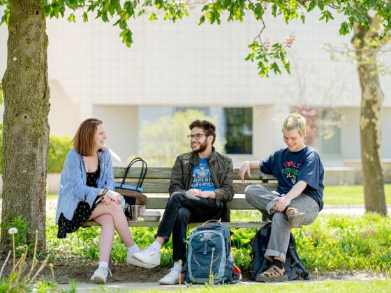 Three students seated on a bench have a friendly conversation.