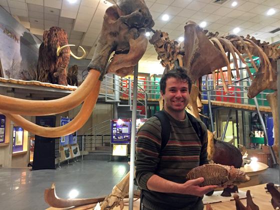 Hank in a museum, with a giant woolly mammoth on display behind him.