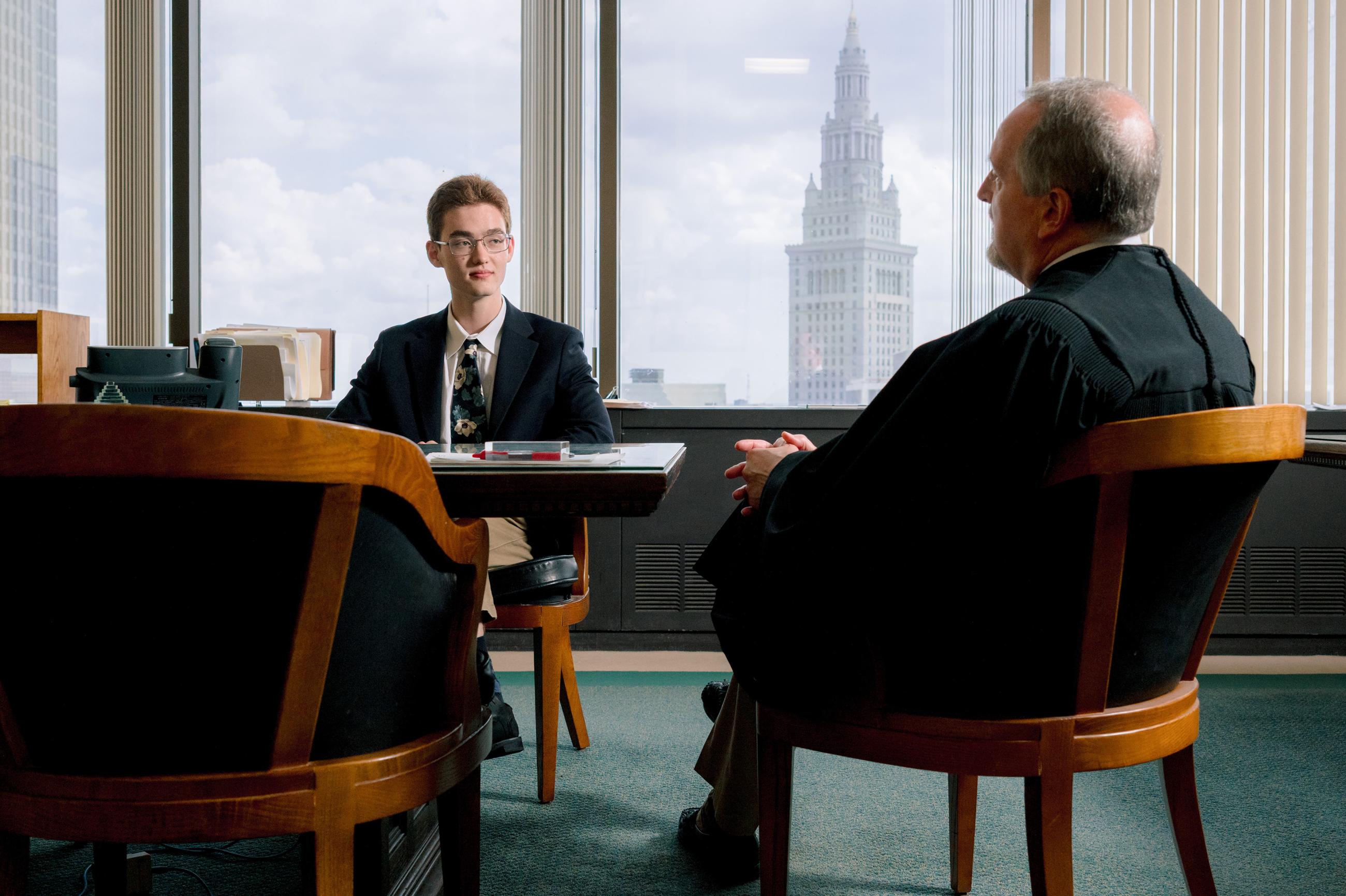 a student wearing a suit coat speaks to a judge as the Cleveland skyline is visible behind them