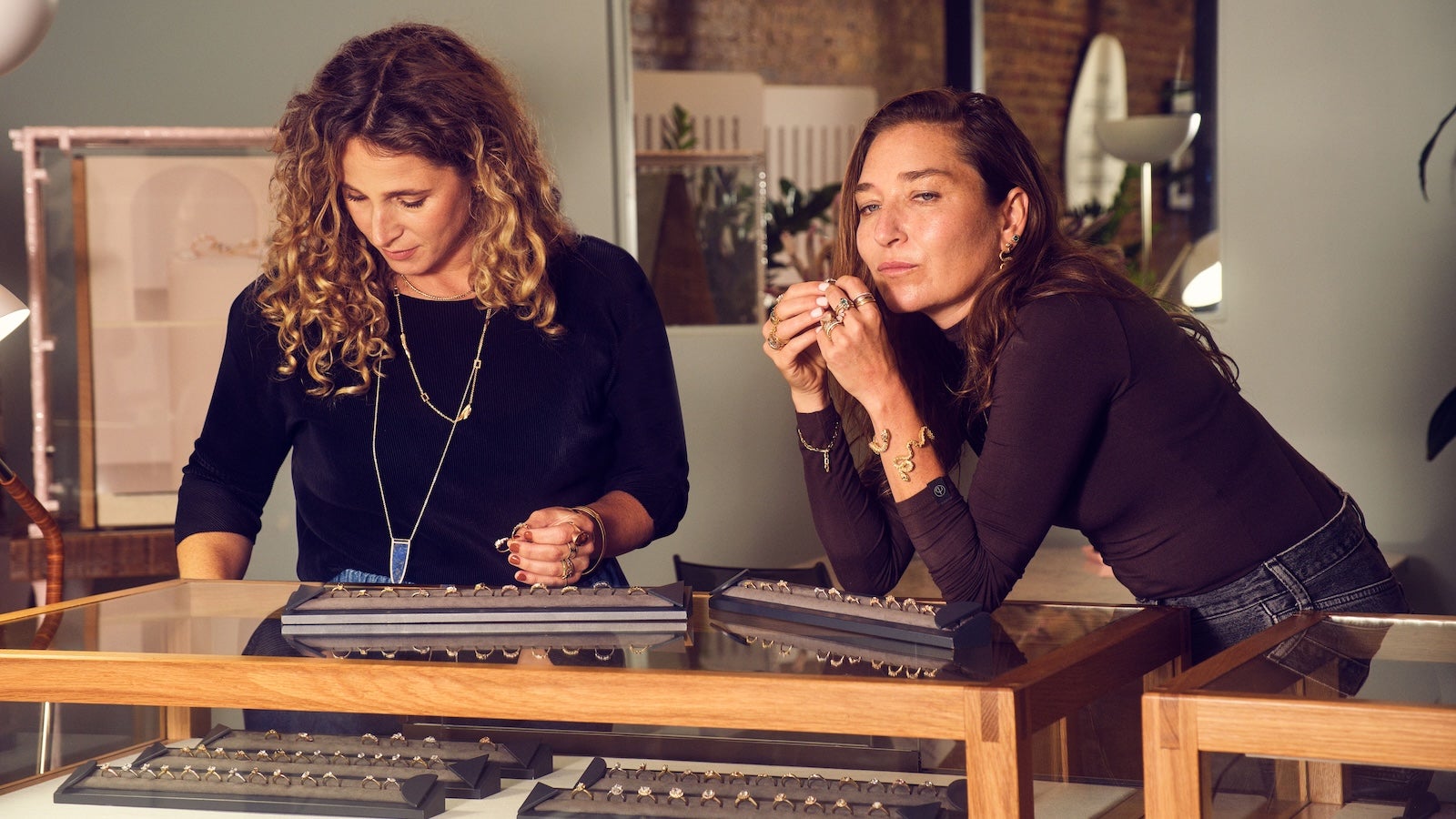 Two women working at a jewelry workbench, examining tools and materials together.