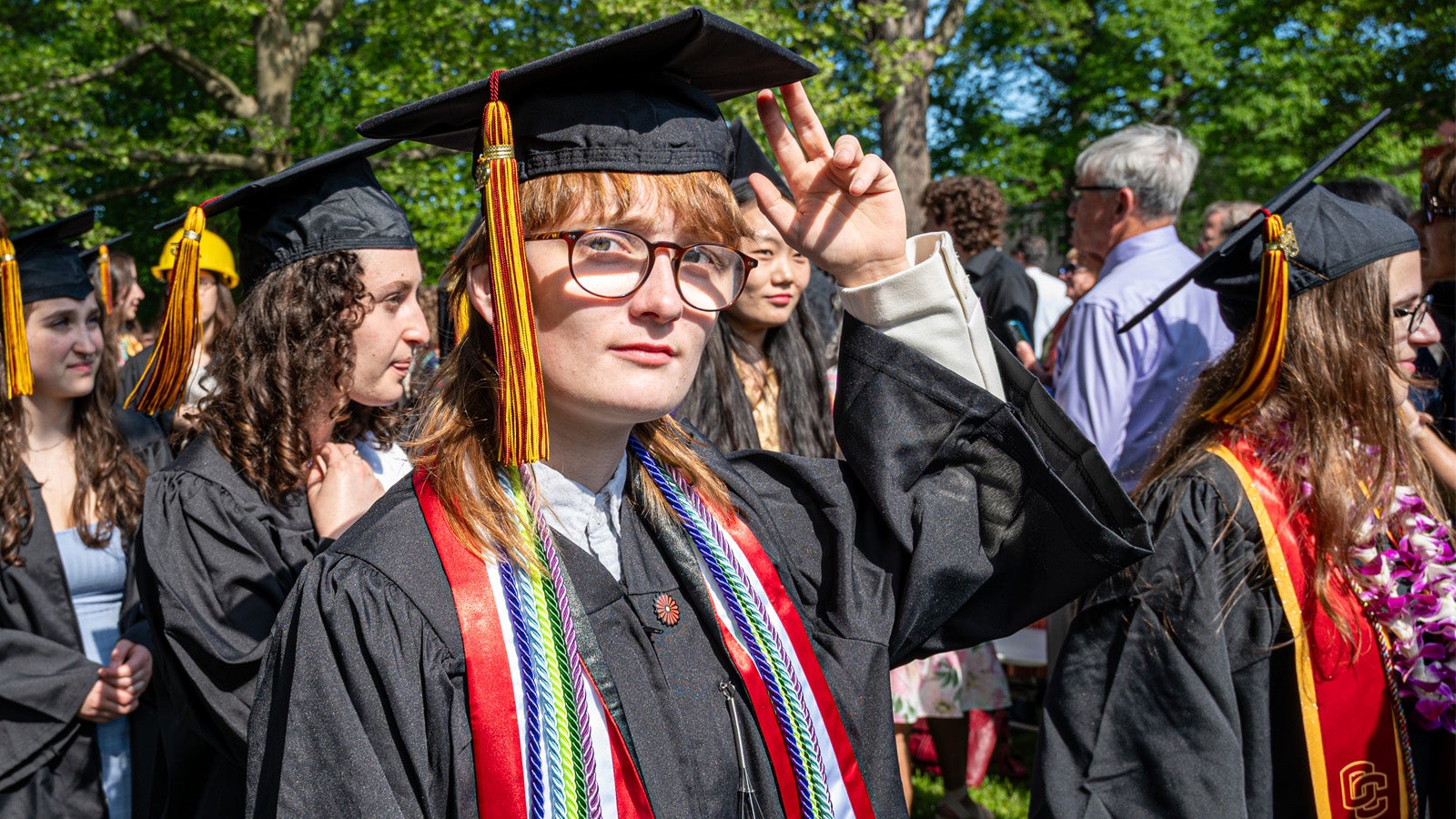 a person wearing a black graduation gown tips their fingers to a mortarboard