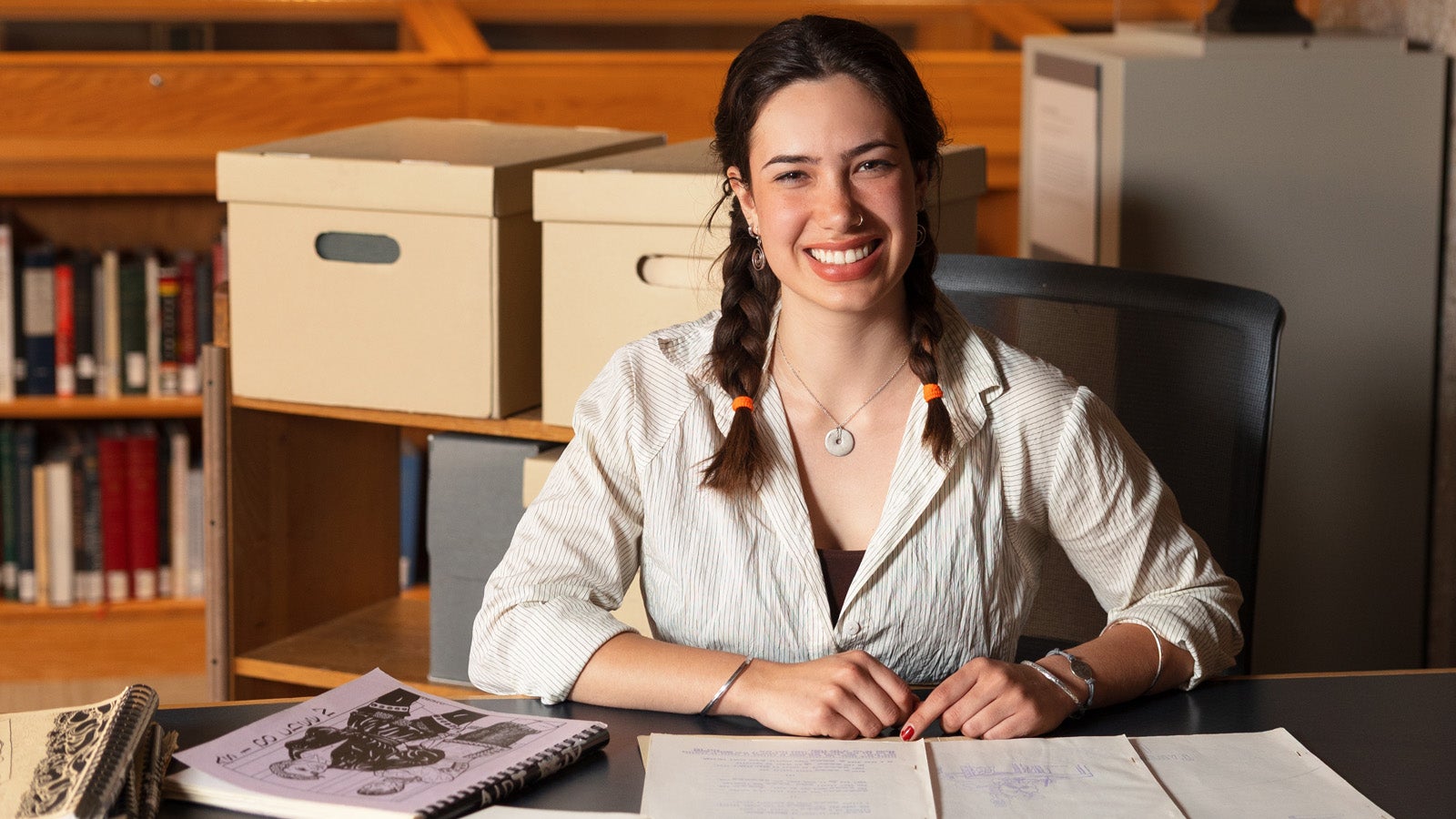 a smiling person wearing a white shirt and braids in a library