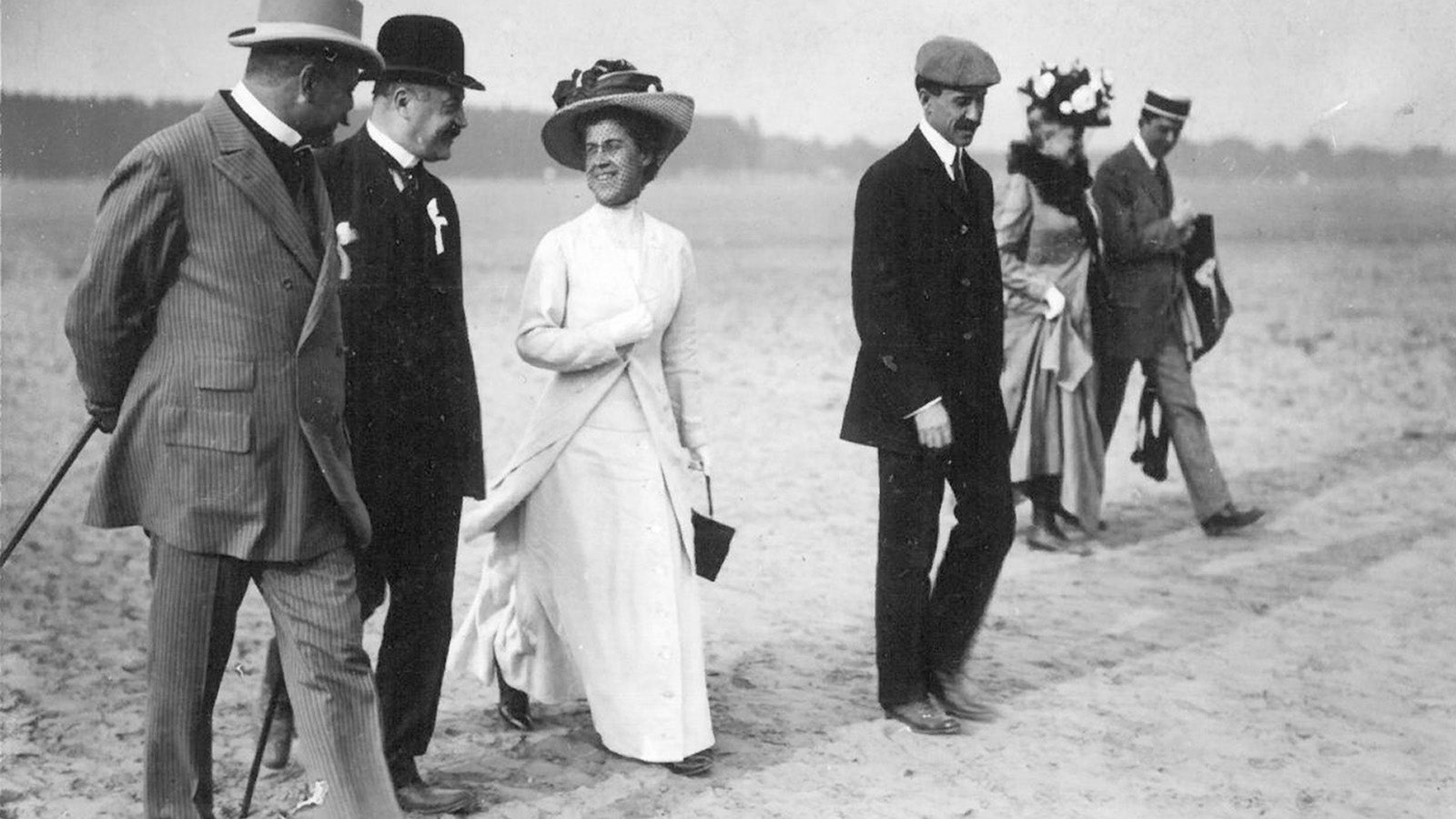 a person from the early 1900s wearing a white dress and hat walking with purpose