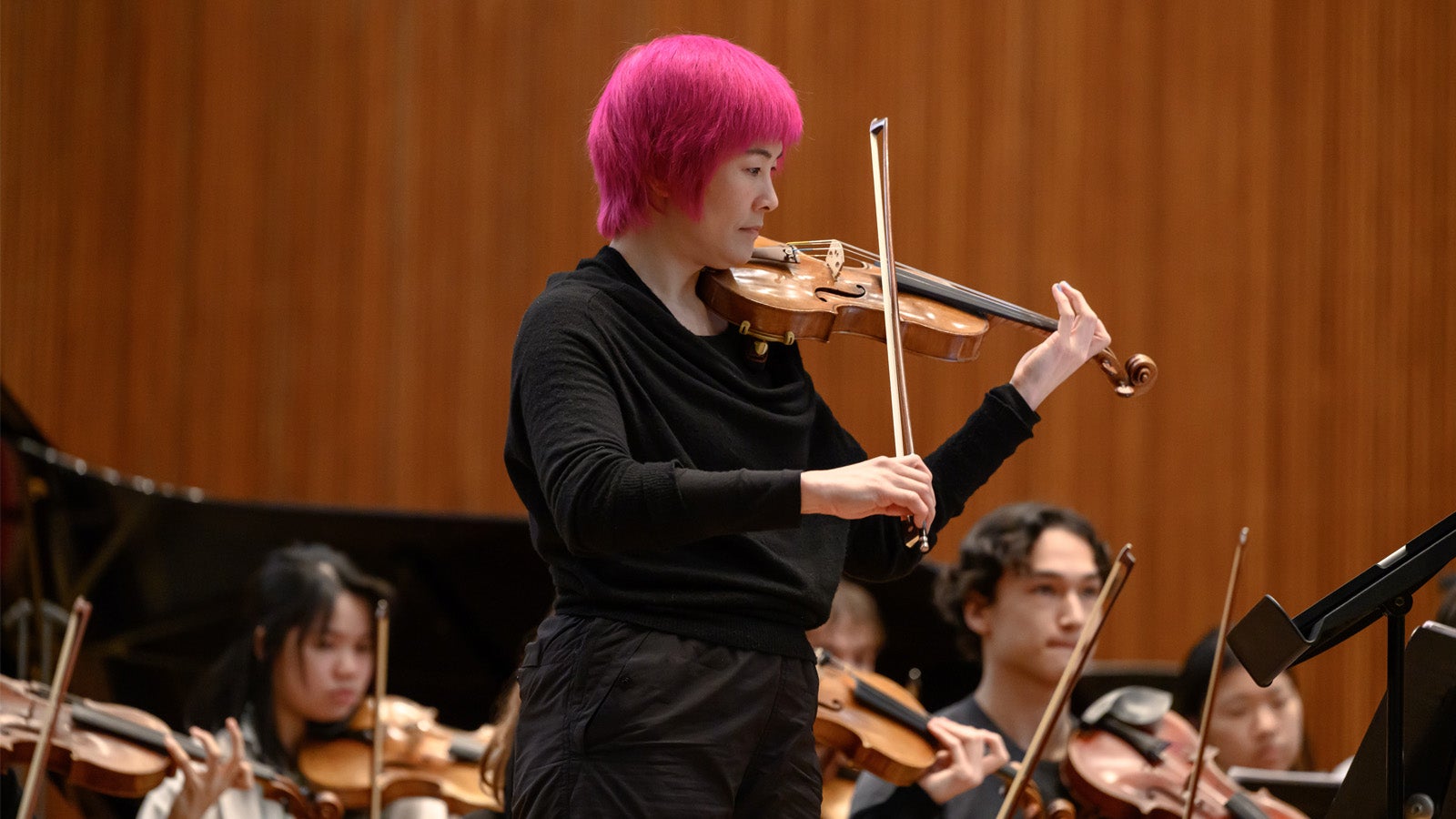 a pink haired violinist plays with student musicians