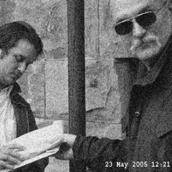 A mysterious man in sunglasses grabs a notebook held by another.
