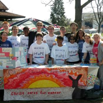 At a table with sign Christ Cares for Cancer stands a group of people wearing tee shirts that say Relay for Life: Hope