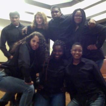 A group of 7 people dressed alike in black shirts and bluejeans