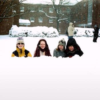 Four people peek over a snowbank