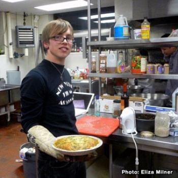 Daniel holds a hot dish in a food service kitchen