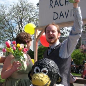 People outdoors with flowers and ballons. One is wearing a monkey head.