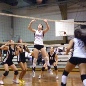 A volleyball player jumps for a ball high above the net