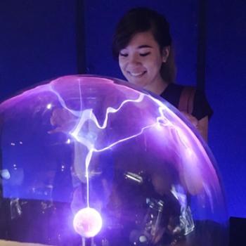 A student touches a transparent globe that contains bolts of electricity