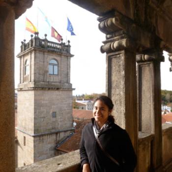 Jessica stands near a medieval turret which is flying flags of Spain and the EU